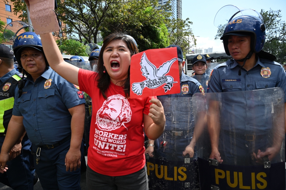 A protester shouts anti-US slogans next to Philippine policemen during a rally in front of the US embassy in Manila on January 6, 2020, demonstrating against the US strike that killed Iranian commander Qasem Soleimani in Iraq. A US drone strike killed top