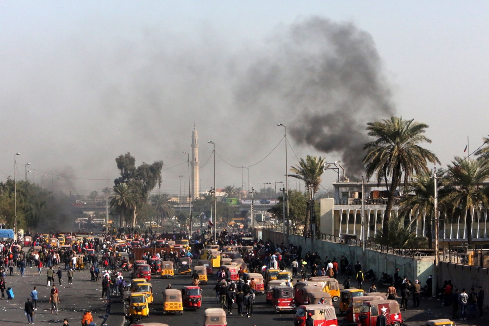 A view of clashes between Iraqi security forces (unseen) and anti-government protesters (foreground) as tuktuks (motorised rickshaws) are present on the scene to transport the injured, at Tayaran Square, east of Tahrir Square in the centre of the capital
