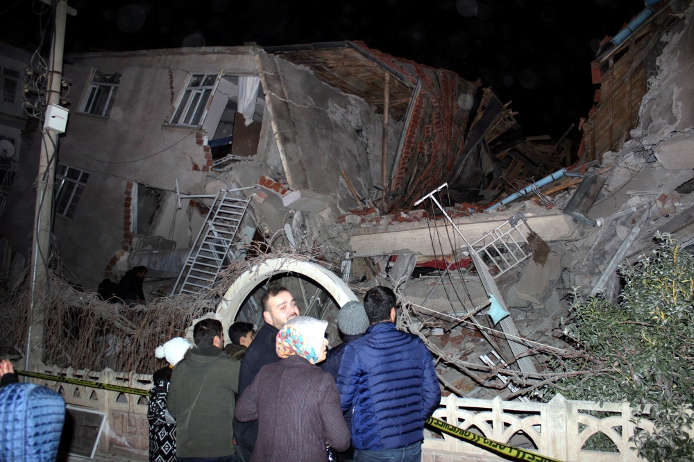 People stand outside a collapsed building after an earthquake in Elazig, Turkey, January 24, 2020. Ihlas News Agency via Reuters