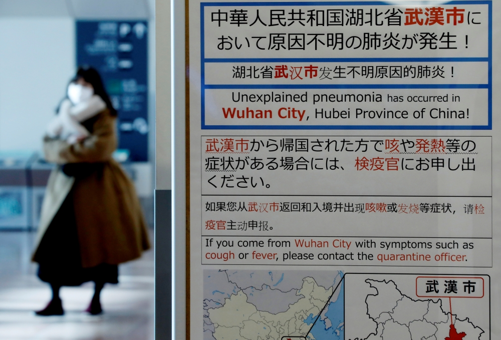 A woman wearing a mask walks past a quarantine notice about the outbreak of coronavirus in Wuhan, China at an arrival hall of Haneda airport in Tokyo, Japan, January 20, 2020. REUTERS/Kim Kyung-Hoon/File Photo 