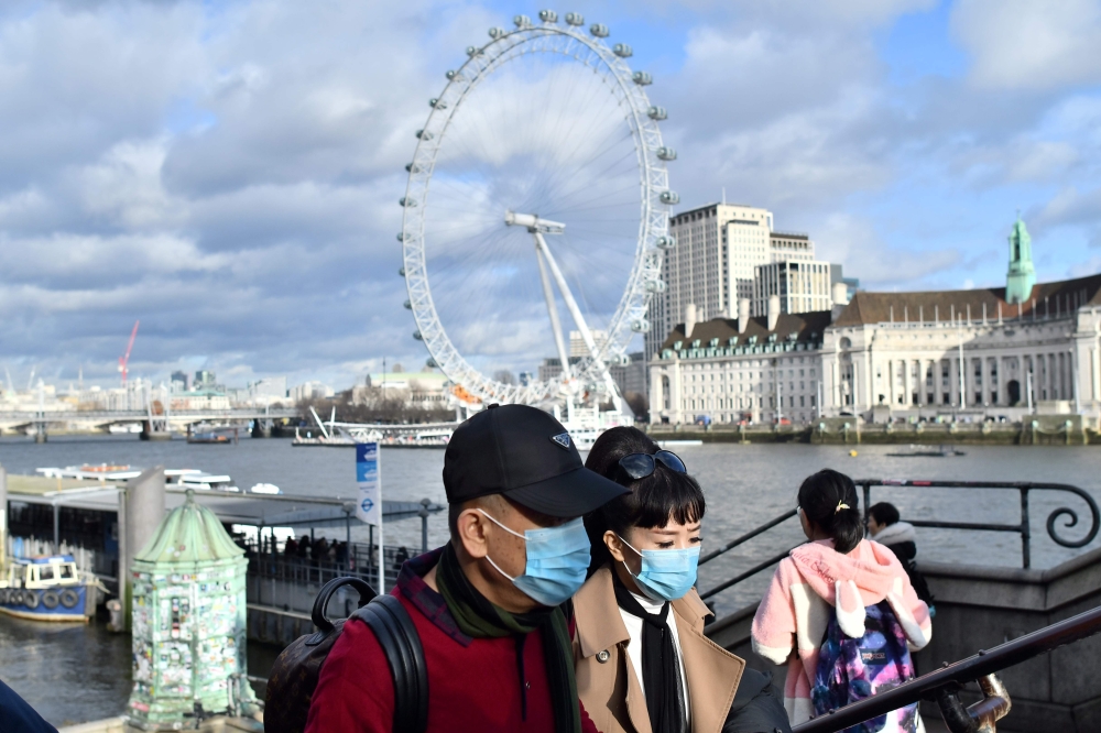 A couple wear face masks as they walk along the Thames embankment in central London on January 28, 2020. Around 1,500 people who came to Britain from the Chinese epicentre of the coronavirus epidemic in the past two weeks must put themselves in isolation,