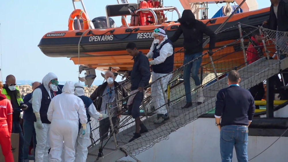 Medical officials wearing protective suits due to the coronavirus outbreak, assist a migrant disembarking from Open Arms rescue ship in Pozzallo, Italy, February 2 2020. Local Team/Reuters TV