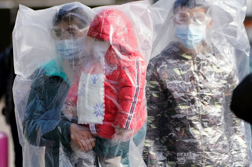 Passengers wearing masks and covered with plastic bags walk outside the Shanghai railway station in Shanghai, China, as the country is hit by an outbreak of a new coronavirus, February 9, 2020. REUTERS/Aly Song