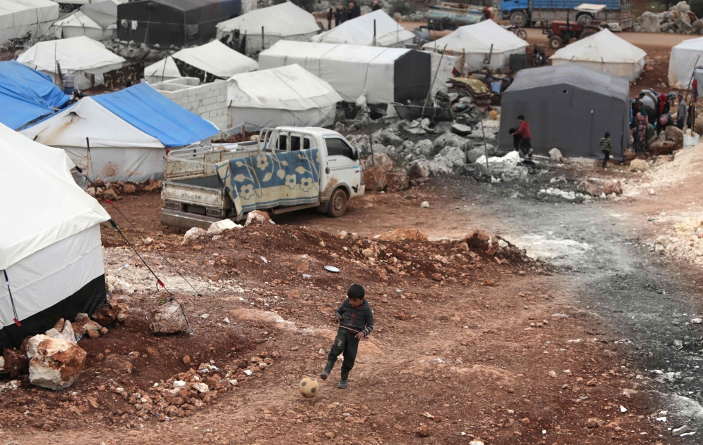 A Syrian boy plays with a football at a makeshift camp for displaced people who fled pro-regime forces attacks in the Idlib and Aleppo provinces, on February 18, 2020. (AFP / Bakr Alkasem)