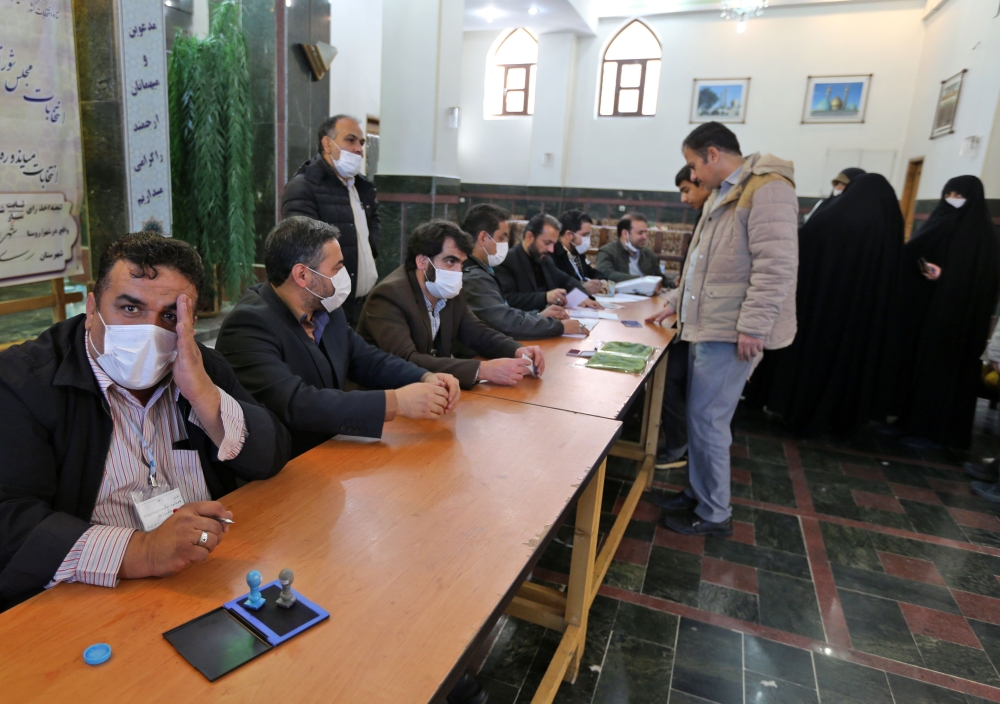 Iranian election officials wear masks as they wait for voters during parliamentary elections at the Shah Abdul Azim shrine on the southern outskirts of Tehran on February 21, 2020./ AFP / ATTA KENARE