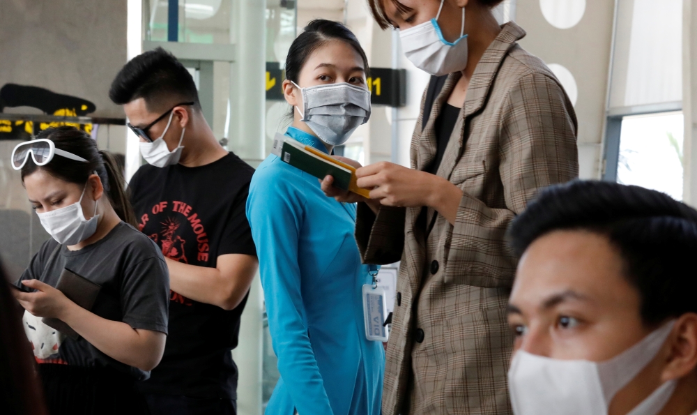 A ground staff member of Vietnam Airlines and passengers wearing a protective mask, following an outbreak of the novel coronavirus, wait for boarding at the Danang airport in Danang city, Vietnam February 23, 2020. REUTERS/Kham