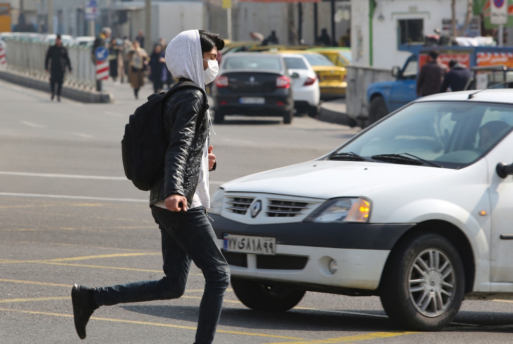A young Iranian man wearing a protective mask, crosses a busy street in the capital Tehran on February 22, 2020.  AFP / ATTA KENARE