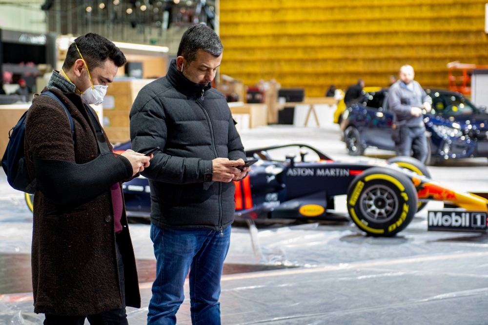 A man wearing a mask stands near a car on February 28, 2020 at the Geneva International Motor Show which has been cancelled due to the Covid-19 epidemic. AFP / Richard Juilliart 
