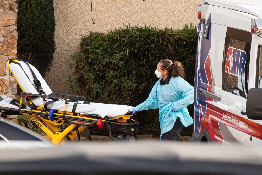 SEATTLE, WA - FEBRUARY 29: A healthcare worker prepares to transport a patient on a stretcher into an ambulance at Life Care Center of Kirkland in Kirkland, Washington. David Ryder/AFP