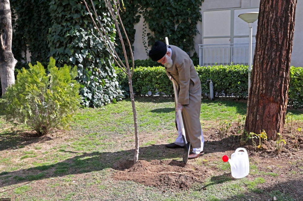 Iran's Supreme Leader Ayatollah Ali Khamenei using a shovel while in the process of planting a tree in a garden during a ceremony marking the week of