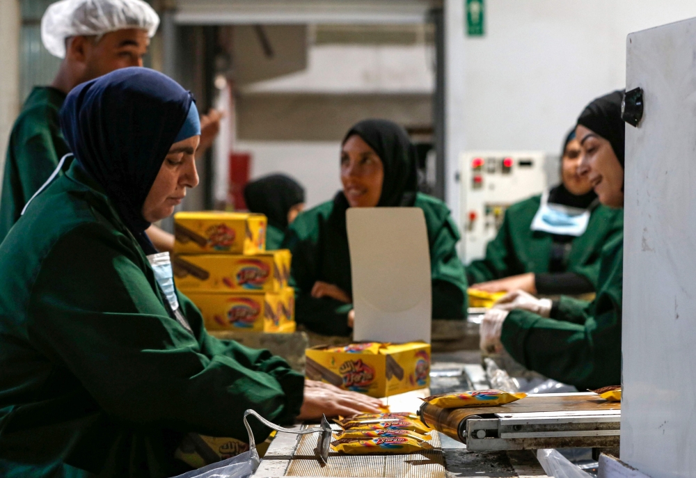 Palestinian industrial workers pack freshly-wrapped wafer biscuits into boxes at a factory in the West Bank city of Ramallah on June 17, 2019. AFP / Abbas Momani