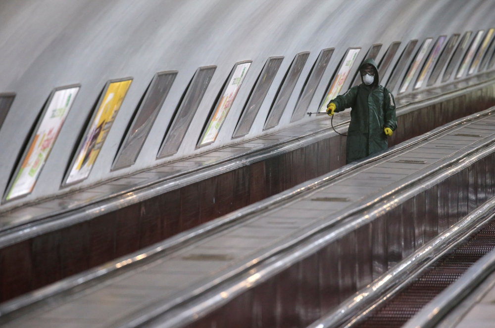 An employee wearing protective gear rides an escalator while spraying disinfectant to sanitize a metro station over coronavirus fears in Tbilisi, Georgia March 3, 2020. REUTERS/Irakli Gedenidze