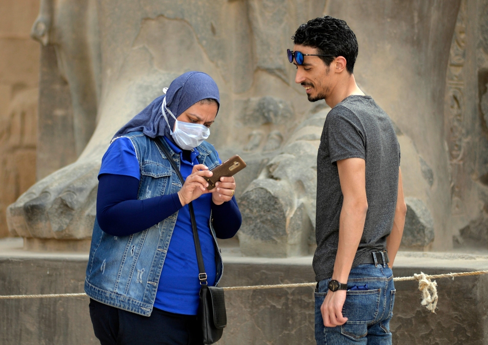 A tourist wearing a protective face mask checks her phone while on a visit to Luxor Temple in Egypt's southern city of Luxor on March 9, 2020. AFP