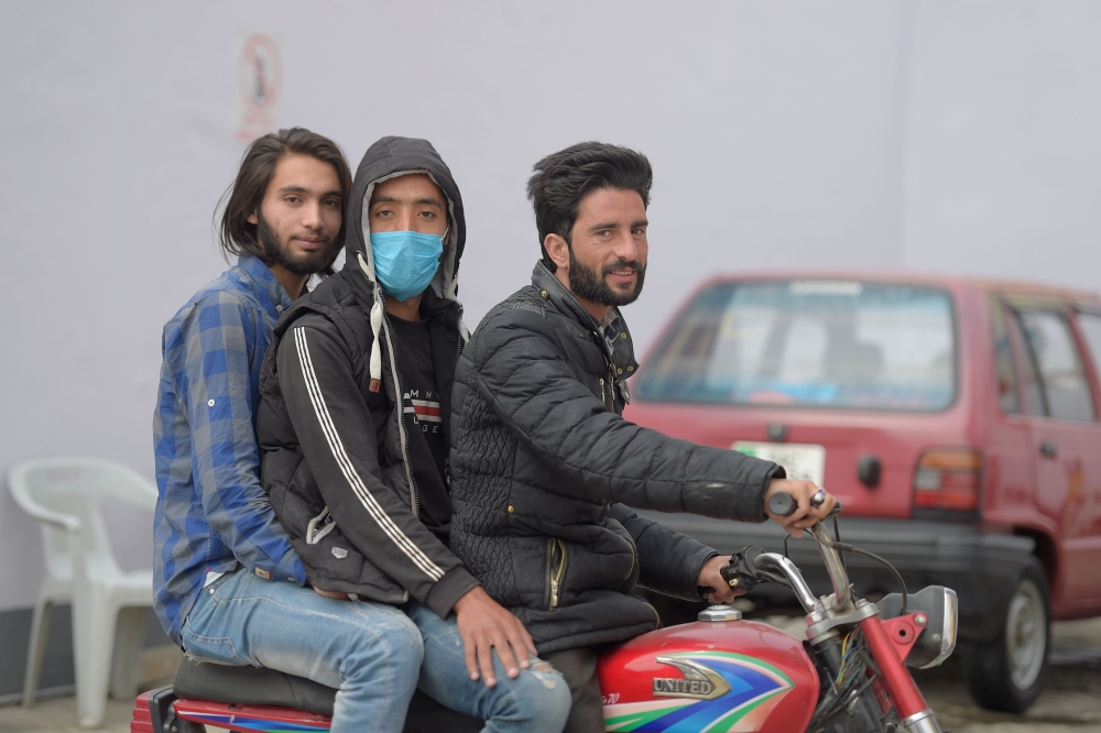A boy wearing a facemask as a preventive measure against the spread of the COVID-19 coronavirus outbreak, rides on a motorbike along with others in Rawalpindi on March 4, 2020.  AFP / Farooq NAEEM 