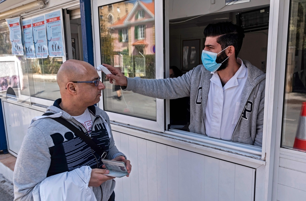 A Cypriot medic checks the temperature of a man crossing the Ledra Palace checkpoint in Nicosia on March 4, 2020. AFP / Iakovos Hatzistavrou