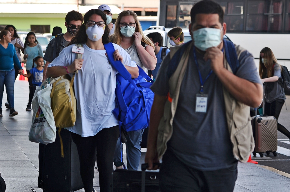 Passengers wear protective face masks to prevent the spread of the new Coronavirus, COVID-19, outside the Toncontin International Airport, in Tegucigalpa, on March 14, 2020. Honduran government has prohibited citizens from Europe, China, Iran, and South K