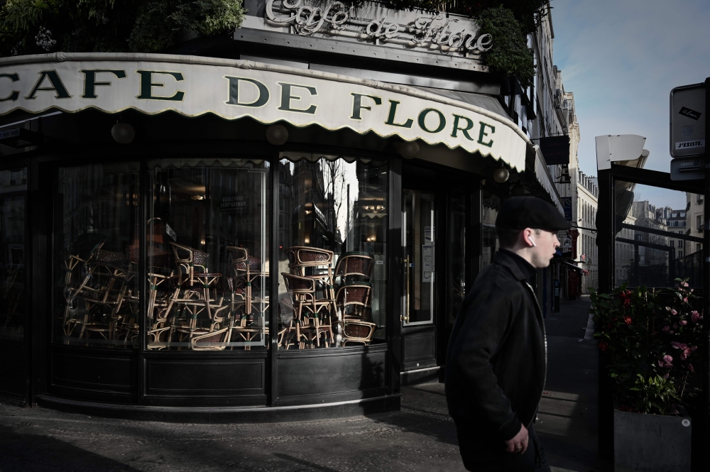 A man walks past the closed Cafe de Flore in Paris' Saint-Germain-des-Pres district on March 15, 2020, as cafes and restaurants are closed amid the COVID-19 outbreak, caused by the novel coronavirus.  AFP / Philippe Lopez 