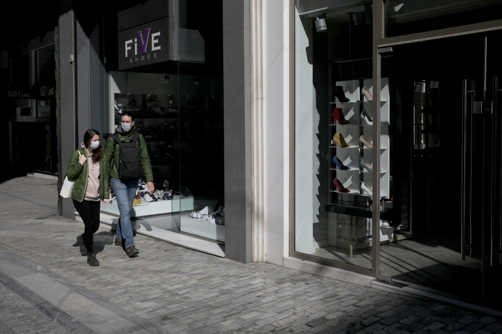 People wear protective face masks as they walk outside closed stores, as a precaution against the spread of the coronavirus disease COVID-19), on the main commercial Ermou Street in Athens, Greece, March 18, 2020. REUTERS/Costas Baltas