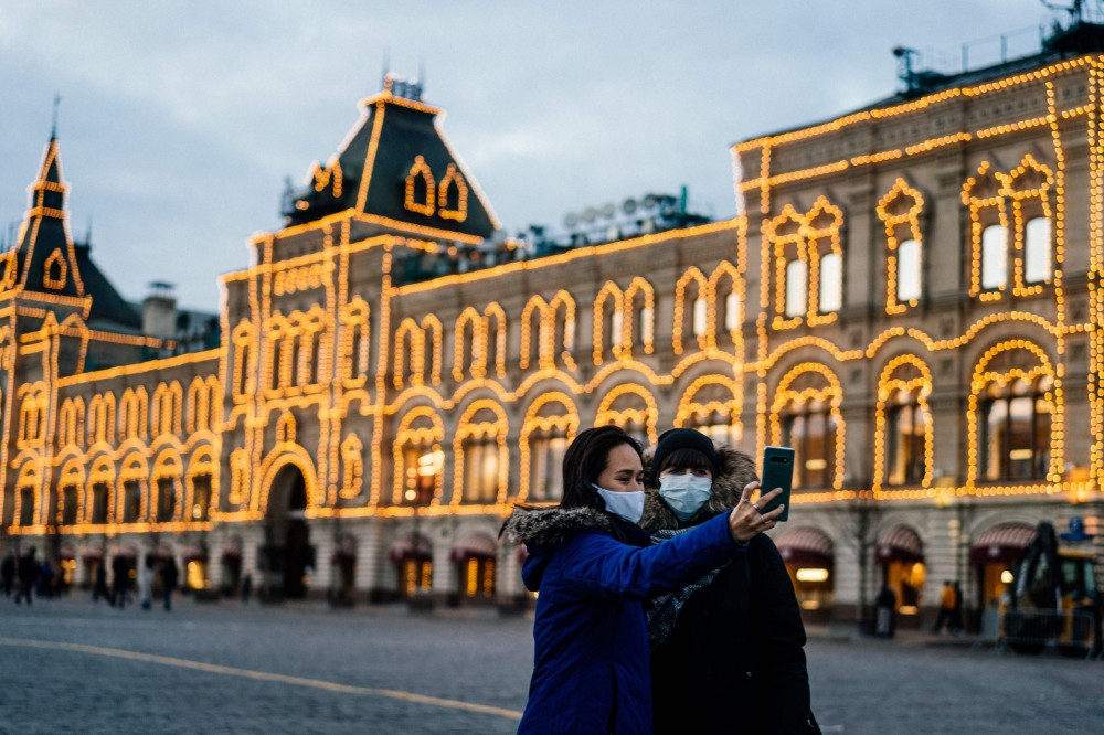 Two women wearing protective face masks to protect from the novel coronavirus, COVID-19, use their smartphone to take a selfie while standing on Red Square in downtown Moscow on March 18, 2020. / AFP / Dimitar DILKOFF
