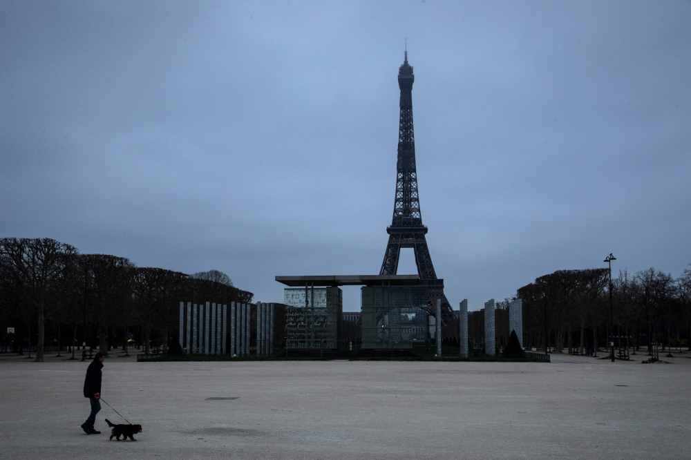 A man walks his dog at the Champs de mars on March 21, 2020 in Paris as a strict lockdown comes into in effect in France to stop the spread of COVID-19, caused by the novel coronavirus. AFP / JOEL SAGET
