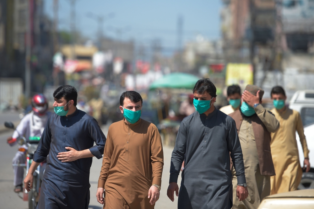 People wearing facemask walks along a road of a closed market area in Rawalpindi on March 22, 2020, after Punjab Province government announced the closing of shops and markets amid concerns over the spread of the COVID-19 novel coronavirus.   / AFP / Faro