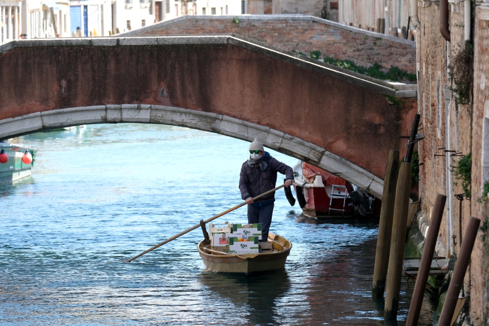 A man delivers fruits and vegetables by rowboat to his customers' houses during the current emergency of the coronavirus disease (COVID-19) in Venice, Italy, March 25, 2020. REUTERS/Manuel Silvestri