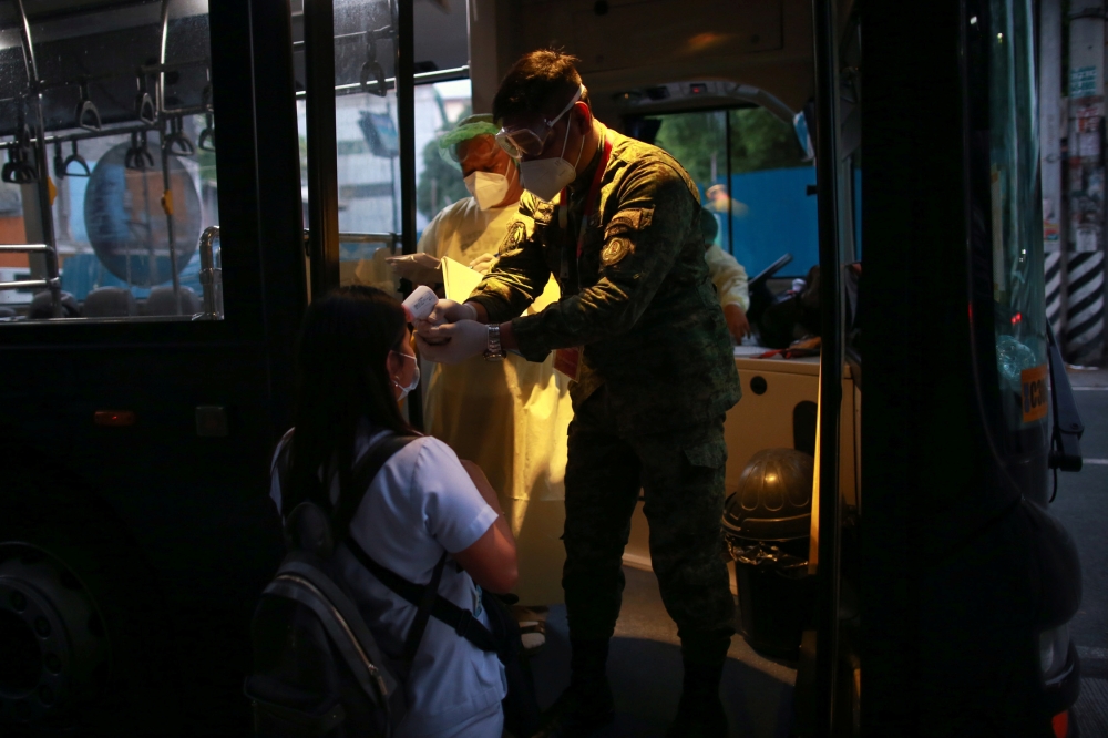 A soldier checks the body temperature of a health worker before entering a free shuttle service following the suspension of mass transportation to contain the spread of coronavirus disease (COVID-19), in Quezon City, Metro Manila, Philippines, March 20, 2