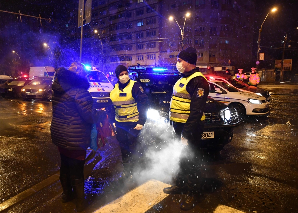 Police forces talk to a pedestrian as they watch over the freshly issued curfew in the streets of Bucharest on March 23, 2020 amid the spread of the COVID-19 (novel coronavirus).  AFP / Daniel MIHAILESCU
