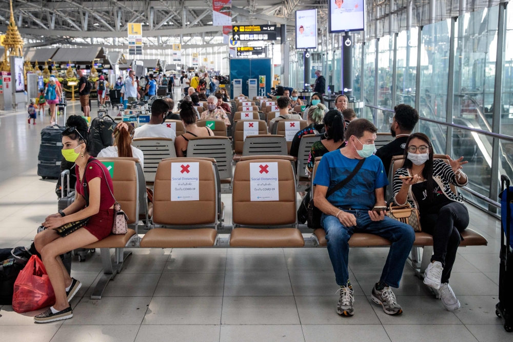 People wearing face masks sit on seats with signs telling travellers where they may sit, in order to observe social distancing rules amid concerns over the spread of the COVID-19 coronavirus, at Suvarnabhumi Airport in Bangkok on March 25, 2020. / AFP / J