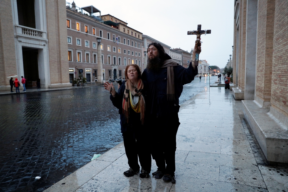 Two persons pray close to the Vatican as Pope Francis delivers an extraordinary 
