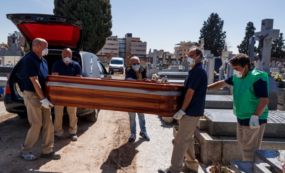 Mortuary employees wearing face masks carry the coffin of a COVID-19 coronavirus victim during a burial at the Fuencarral cemetery in Madrid on March 29, 2020. AFP / Baldesca Samper
  