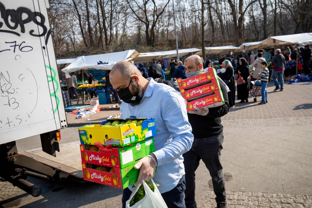 Saturday shoppers wearing protection masks carry their goods at the Yorck Strasse market in Berlin on March 28, 2020 amid the novel coronavirus pandemic. . / AFP / Odd ANDERSEN