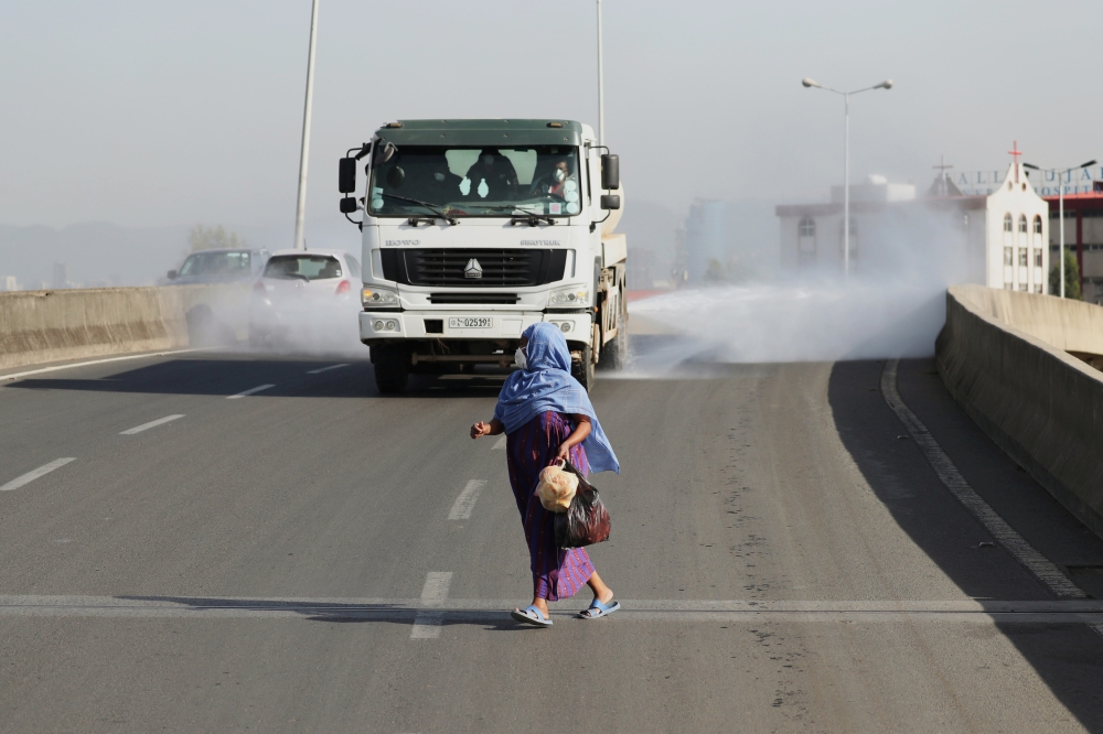 A woman wearing a face mask, runs in front of a truck spraying disinfectant on the street as part of the COVID-19 prevention measures in Addis Ababa, Ethiopia March 29, 2020. Reuters/Tiksa Negeri
 