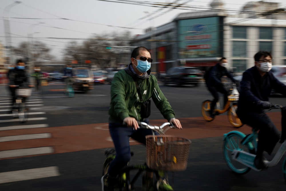 People wearing face masks ride bicycles on a street following an outbreak of the coronavirus disease (COVID-19), in Beijing, China March 30, 2020. REUTERS/Carlos Garcia Rawlins