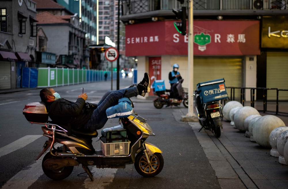 Delivery men wwearing a wearing a facemask as a preventive measure against the COVID-19 coronavirus wait for mobile orders along a street in Wuhan, in China's central Hubei province on April 1, 2020. / AFP / NOEL CELIS