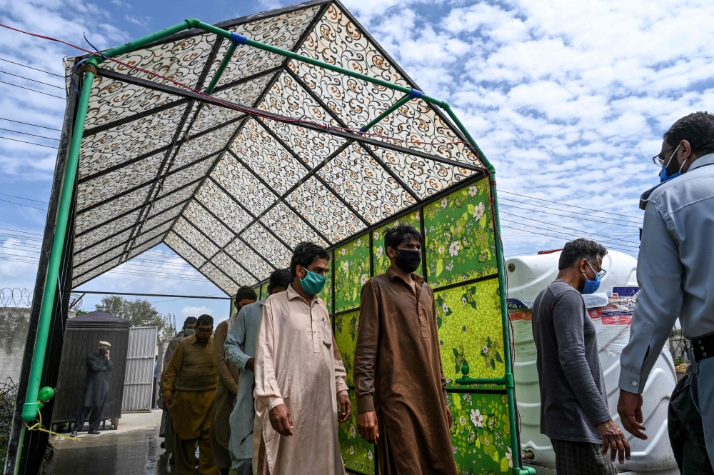 Residents wearing facemasks walk through a disinfecting tunnel at a vegetable and fruit market during a government-imposed nationwide lockdown against the COVID-19 coronavirus, in Islamabad on April 1, 2020. / AFP / Aamir QURESHI
