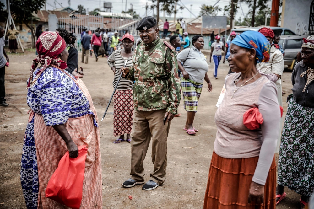 A Kenyan Police officer explains the physical distancing measures that have to be followed to a group of people affected by the measures adopted by the Kenyan Government to stop the spread of COVID-19 coronavirus while they wait for boxes with food and ot