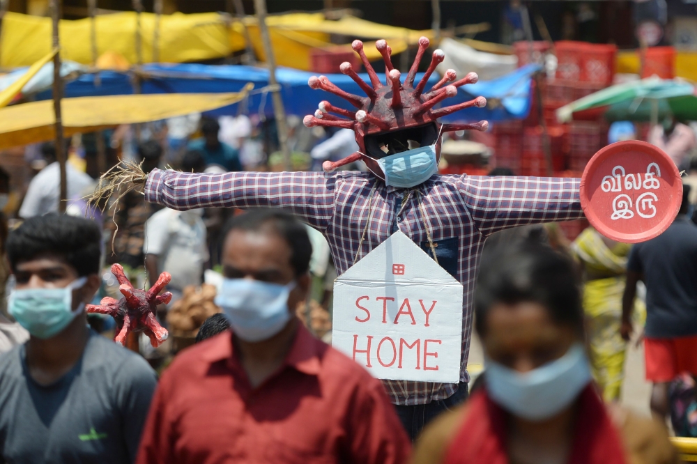 People walk past a Covid-19 awareness scarecrow placed by Chennai municipality at a market during a government-imposed nationwide lockdown as a preventive measure against the COVID-19 coronavirus, in Chennai on April 11, 2020. / AFP / Arun SANKAR