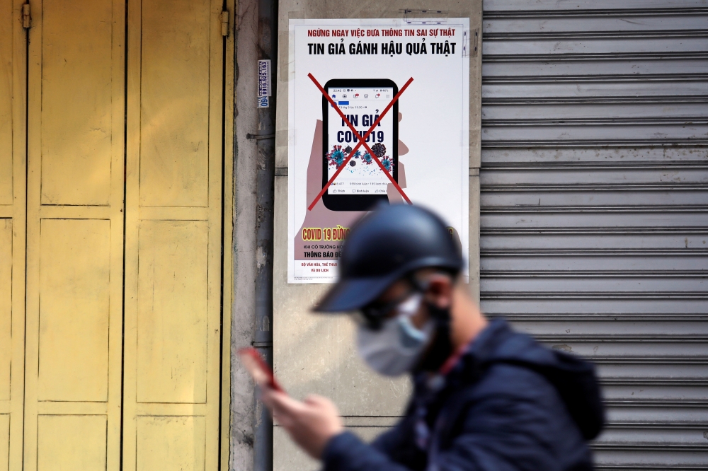 A man uses a smartphone as he walks past a poster warning against spreading 'fake news' on the coronavirus in Hanoi, Vietnam April 14, 2020. Picture taken April 14, 2020. REUTERS/Kham
