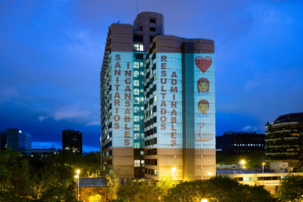 :A projection from a private house illuminates the facade of the Barcelona Hospital reading 