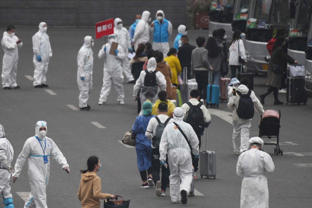 Travelers arriving from Wuhan are escorted to buses which will take them to their quarantine locations, at Beijing West Railway Station on April 15, 2020. / AFP / GREG BAKER
