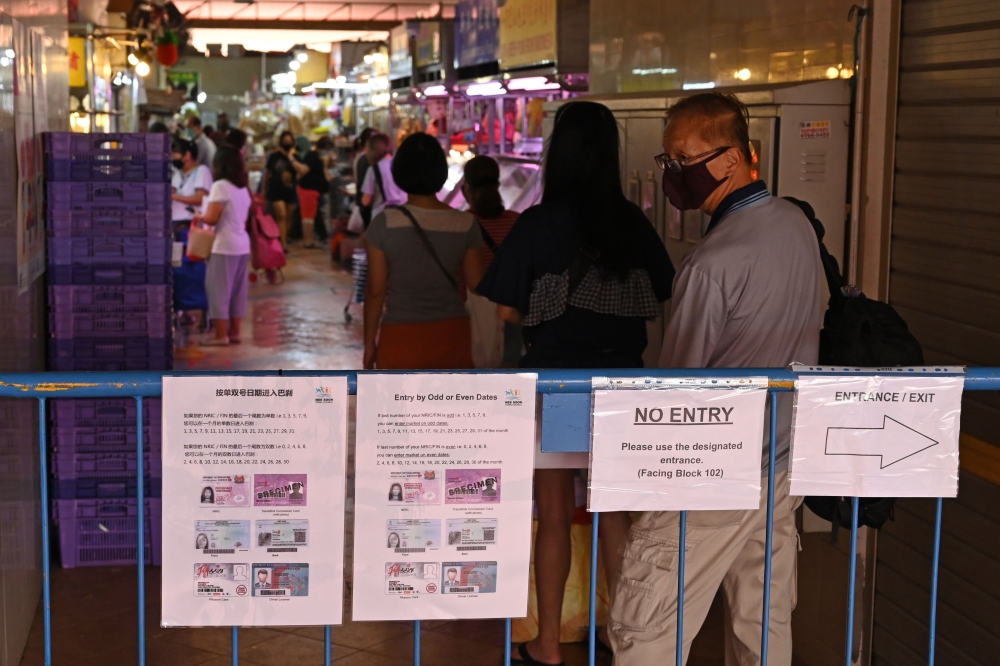 Instruction notice placards hang on a barrier as a man wearing a facemask as a prevention measure against the spread of the COVID-19 coronavirus queues to enter a wet market in Singapore on April 22, 2020. / AFP / ROSLAN RAHMAN