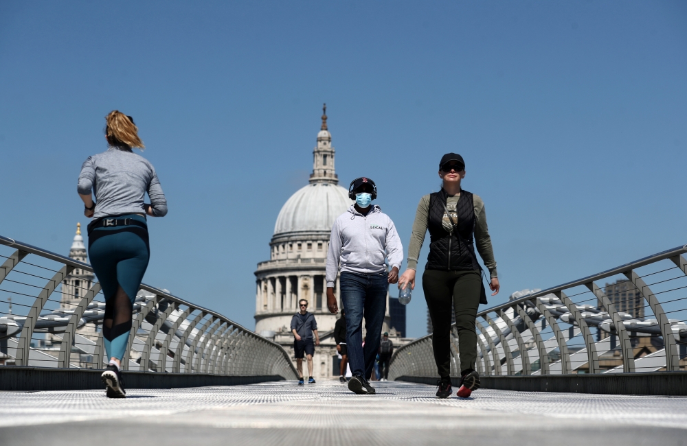 A man wearing a face mask crosses Millennium Bridge, as the spread of the coronavirus disease (COVID-19) continues, in London, Britain, April 25, 2020. REUTERS/Simon Dawson