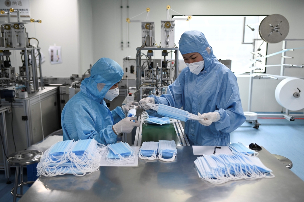 Two workers wearing protective suits check masks at Naton Medical Group, a company which makes medical equipment in Beijing on April 24, 2020. / AFP / WANG ZHAO
