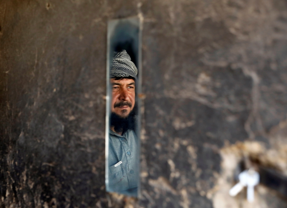 A man is reflected in a mirror as he looks at policemen near the shops during the coronavirus disease (COVID-19) outbreak in Kabul, Afghanistan April 23, 2020.REUTERS/Mohammad Ismail