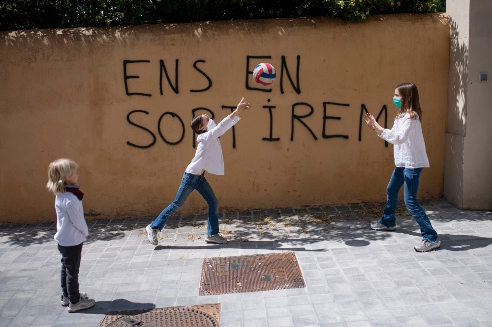 Jan, 5, looks at his sisters Ines, 11, and Mar (C), 9, playing in front of a graffit reading in Catalan 