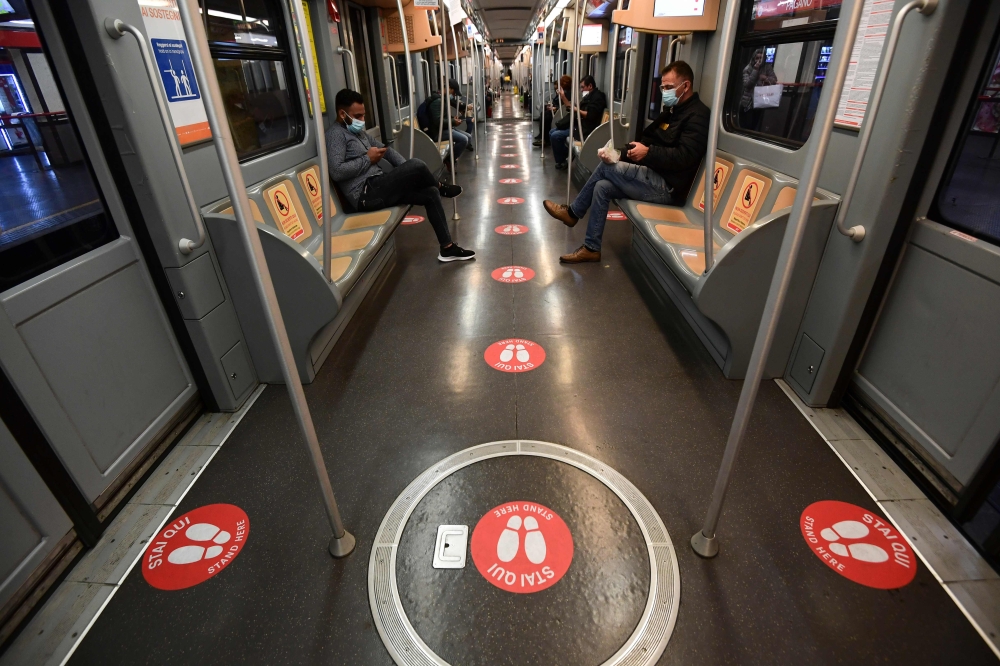 Commuters maintaining distance sit next to seats with stickers reading 