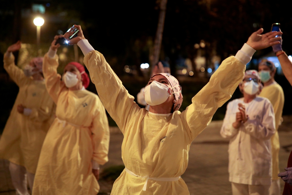 FILE PHOTO: Health workers gesture as citizens show their support from their balconies and windows, amid the spread of the coronavirus disease (COVID-19), in Barcelona, Spain April 15, 2020. REUTERS/Nacho Doce/File Photo