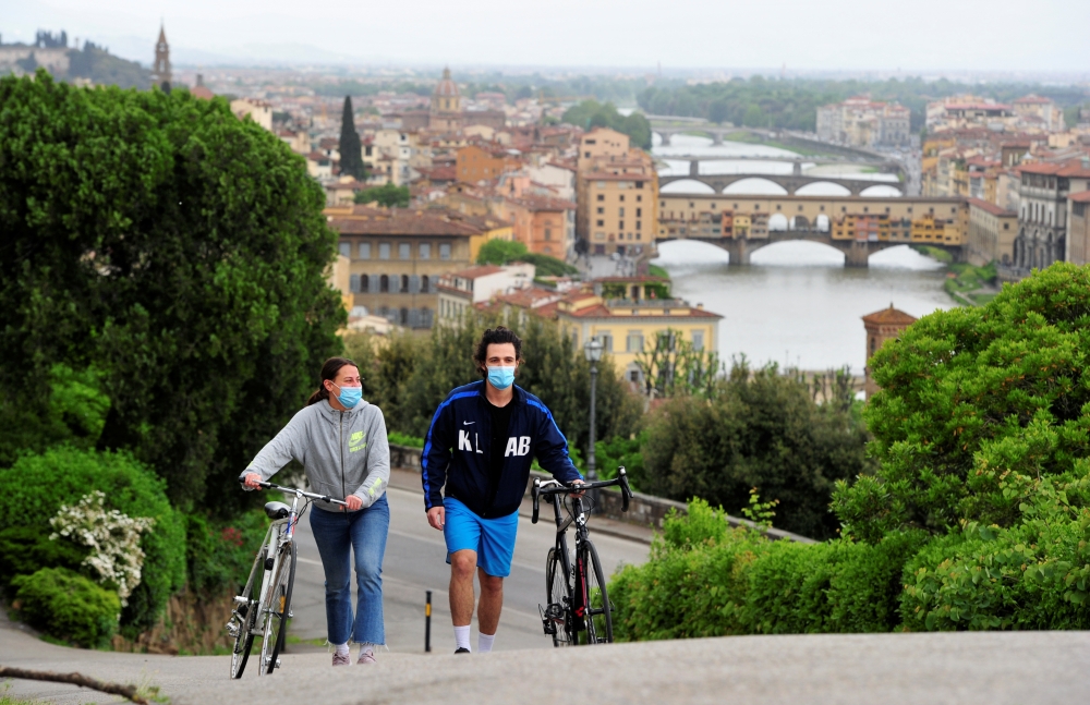 People wearing protective face masks push their bicycles during the lockdown, ahead of Italy's gradual lifting of restrictions which begins from May 4, due to the spread of the coronavirus disease (COVID-19), in Florence, Italy, May 1, 2020. REUTERS/Jenni