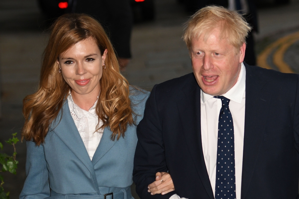 (FILES) In this file photo taken on September 28, 2019 Britain's Prime Minister Boris Johnson (R) walks with his partner Carrie Symonds as they arrive at The Midland, near the Manchester Central convention complex in Manchester, northwest England . AFP / 